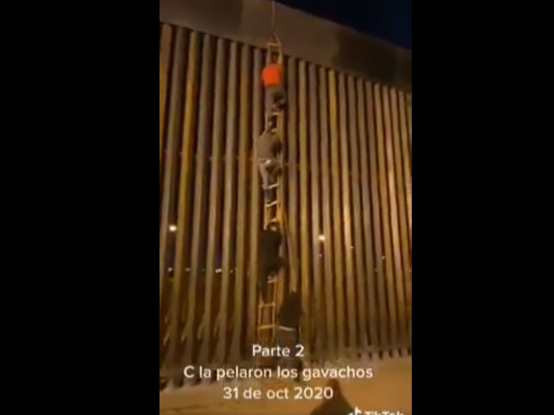 Toma del momento en el que los hombres saltan el muro fronterizo.
