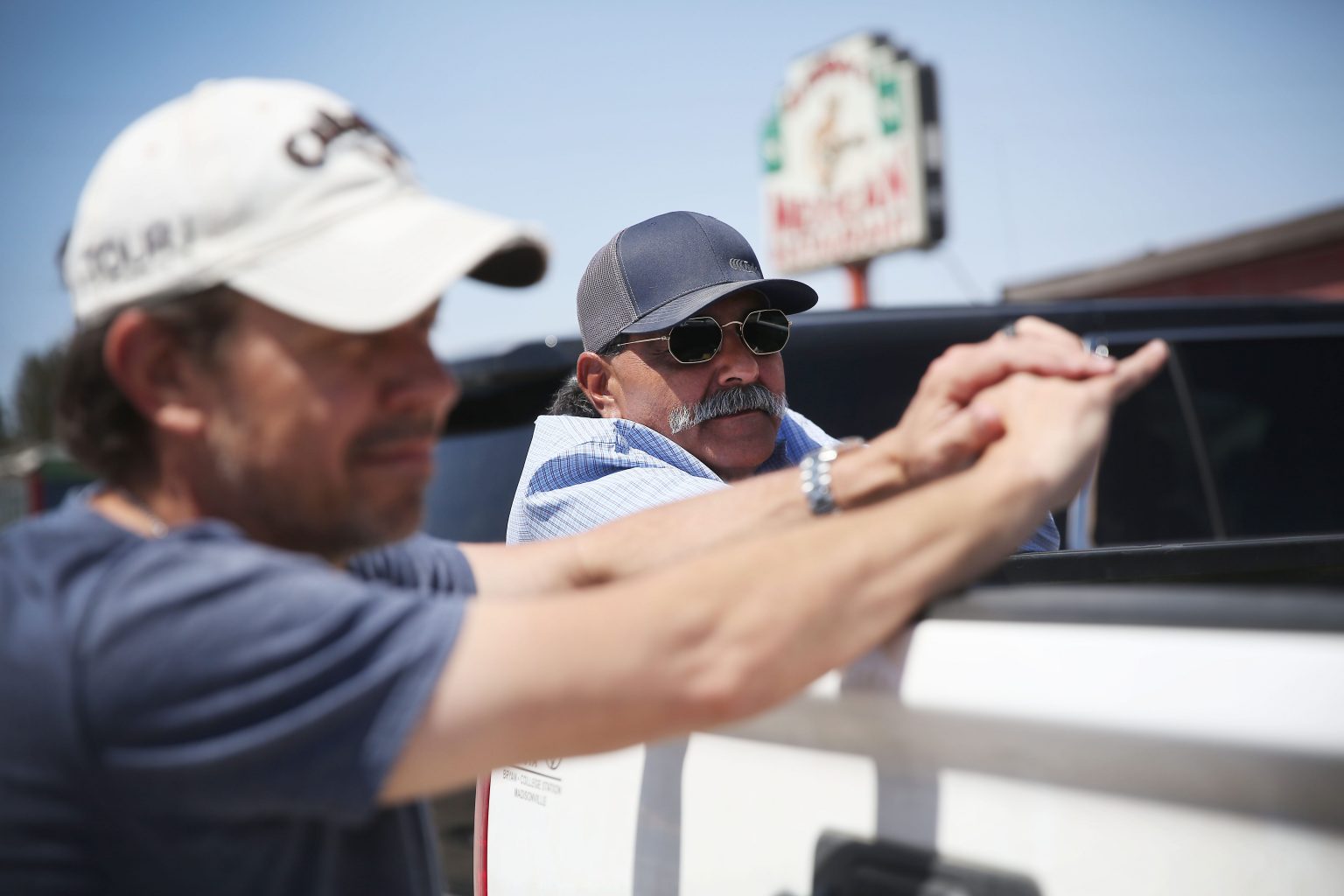 Richard Orona, derecha, y Bert Montee, izquierda, hablan sobre lo que han oído al respecto del refugio de niños migrantes, fuera del restaurante mexicano Alfredo’s en Pecos. | Foto: Briana Sánchez.
