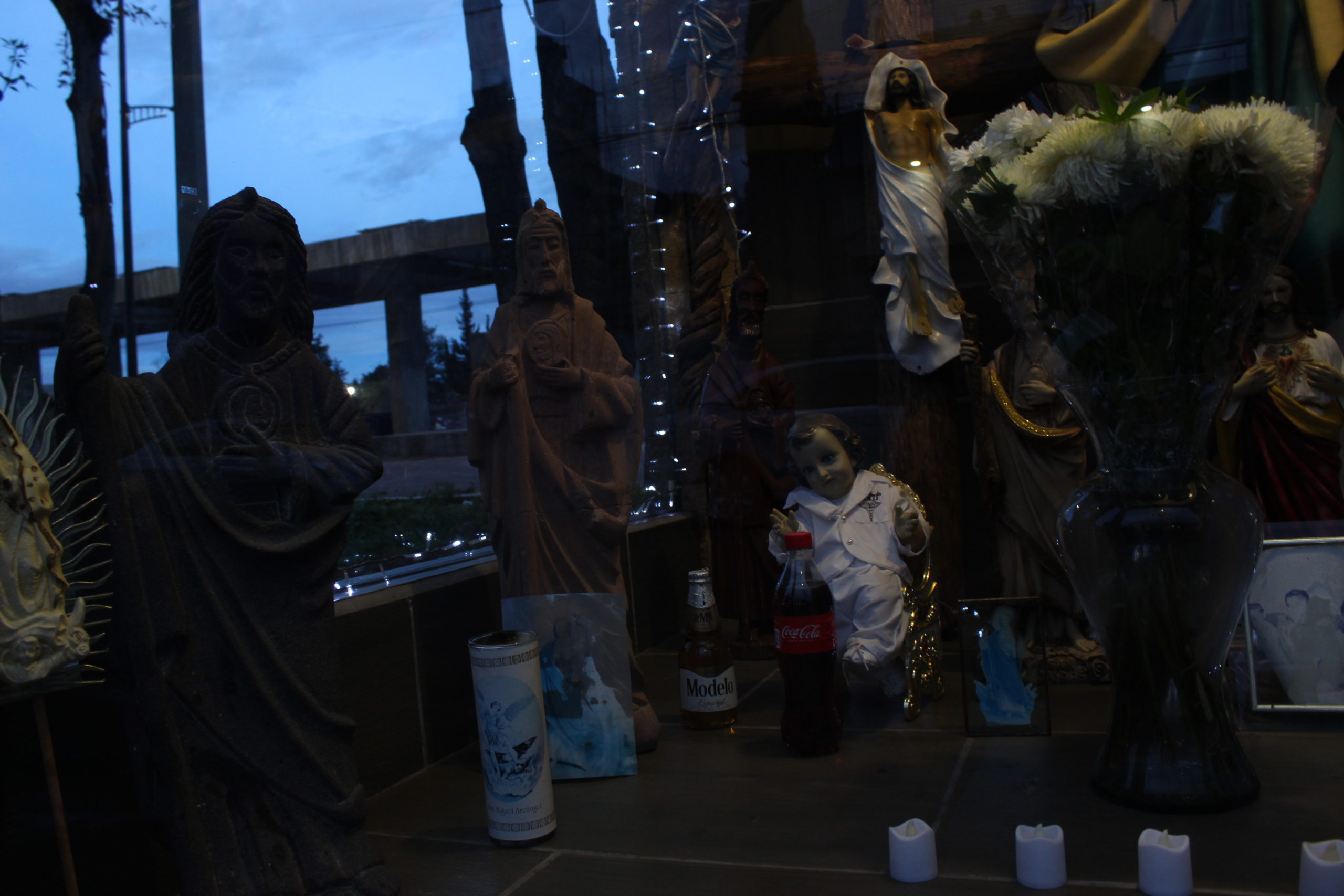 En esta capilla se encuentran diversas maneras de entregarle respeto a la gente fallecida de la colonia. Una de estas muestras es colocar en el altar las bebidas favoritas de los difuntos. | Foto: Iván Berriel / Conexión Migrante.