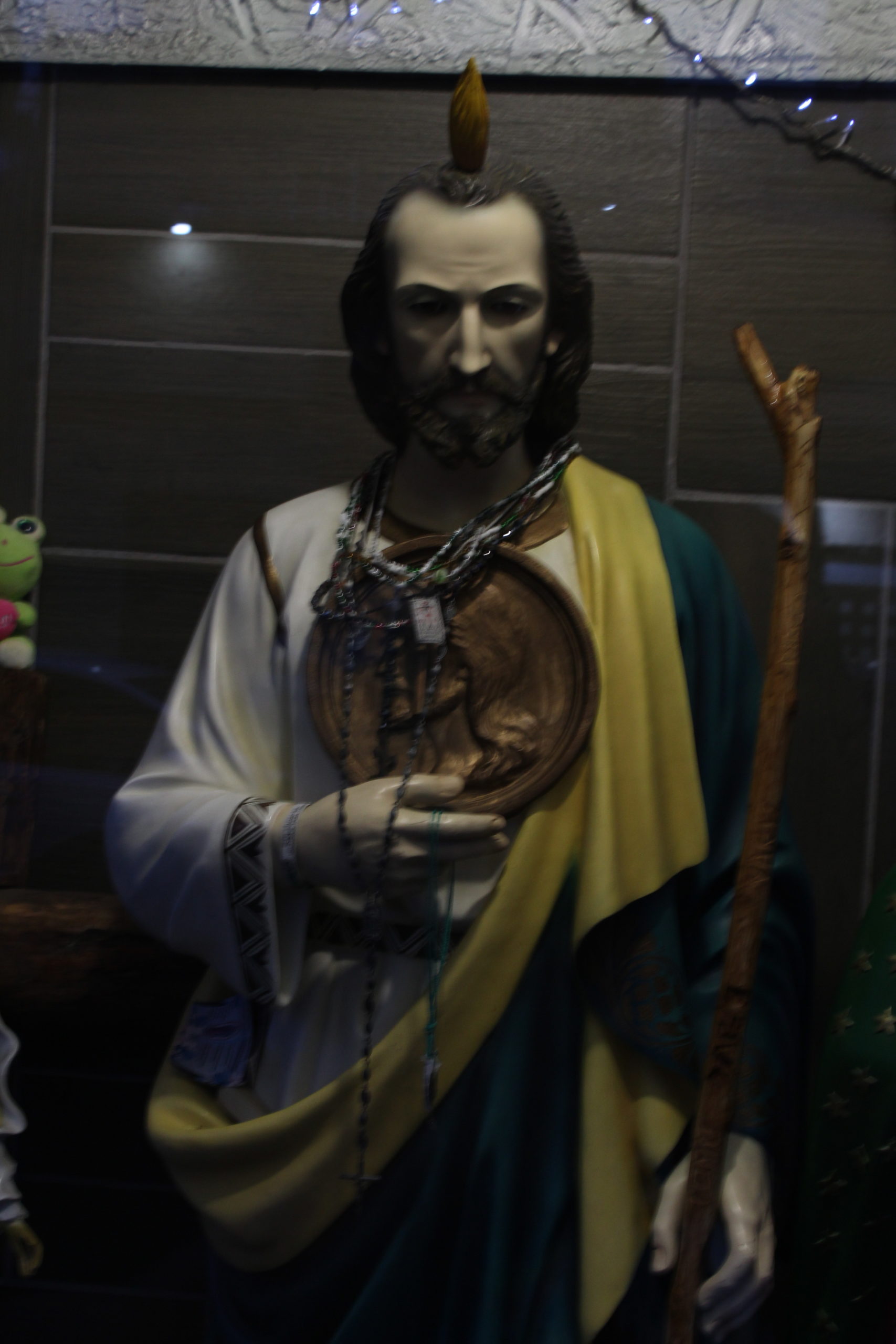 El bastón de madera de esta imagen de San Judas fue tallado por dos hermanos que, desgraciadamente, perdieron la vida en un accidente. Ahora sus familiares cuidan de esta pequeña capilla; también han ayudado a personas migrantes que van de tránsito por la CDMX. | Foto: Iván Berriel / Conexión Migrante.