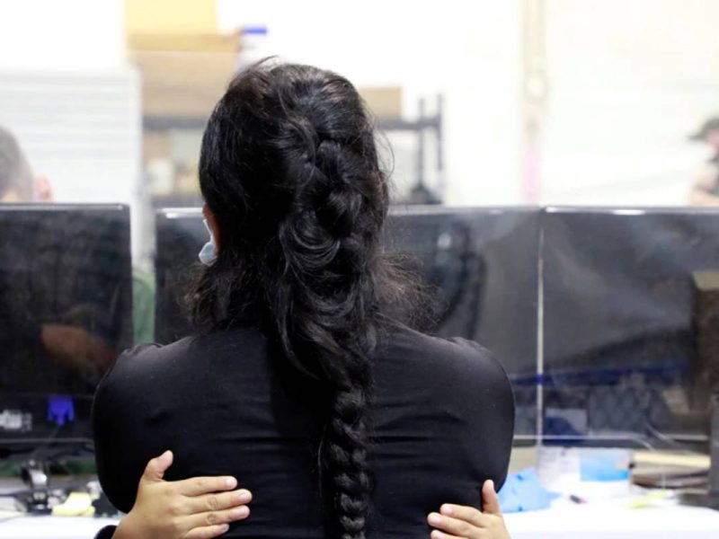 Una mujer migrante es abrazada por un niño dentro de una instalación de procesamiento temporal para migrantes, incluidos menores no acompañados