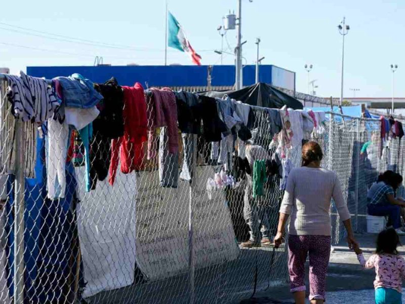 Migrantes caminan junto a la cerca de un campamento improvisado que bloquea la entrada a un cruce peatonal a Estados Unidos el 8 de noviembre de 2021, en Tijuana, México.