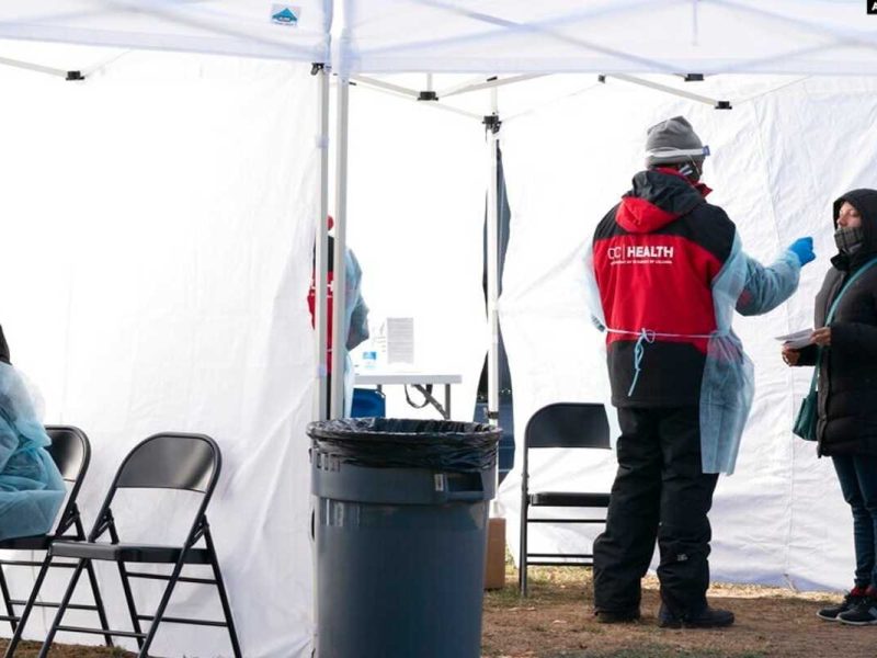 Un trabajador, a la izquierda, descansa por un segundo entre pacientes, mientras otra persona, a la derecha, se hace la prueba de COVID-19 en un sitio de test sin cita previa en Farragut Square, el jueves 23 de diciembre de 2021, a pocas cuadras de la Casa Blanca, en Washington.
