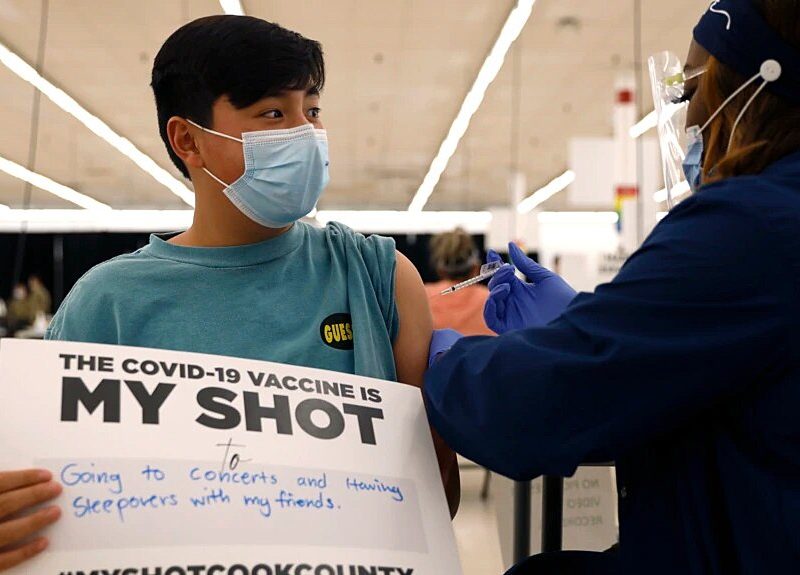 Un niño de 13 años muestra un cartel de apoyo a la vacunación mientras recibe su primera dosis en Illinois, en mayo de 2021.