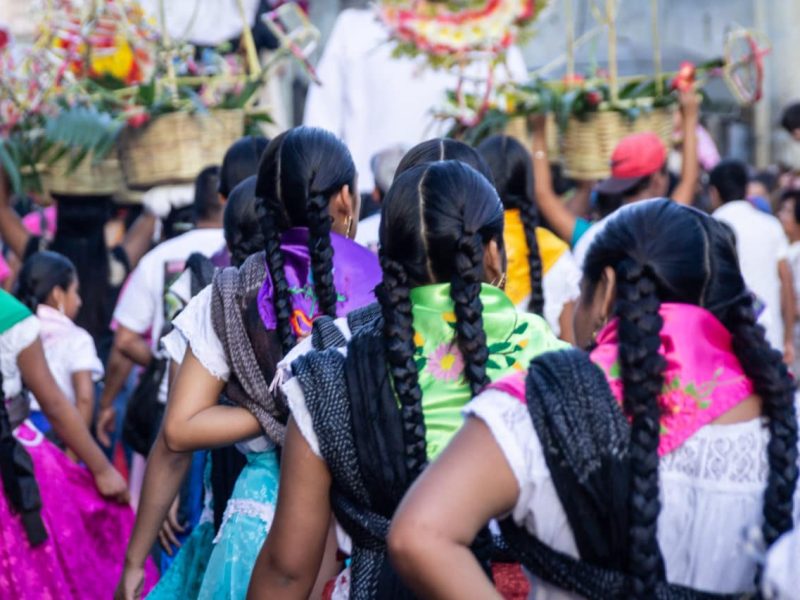 Espaldas de mujeres indígenas mexicanas con trenzas y rebozos de colores en la fiesta de la Guelaguetza en Oaxaca, México