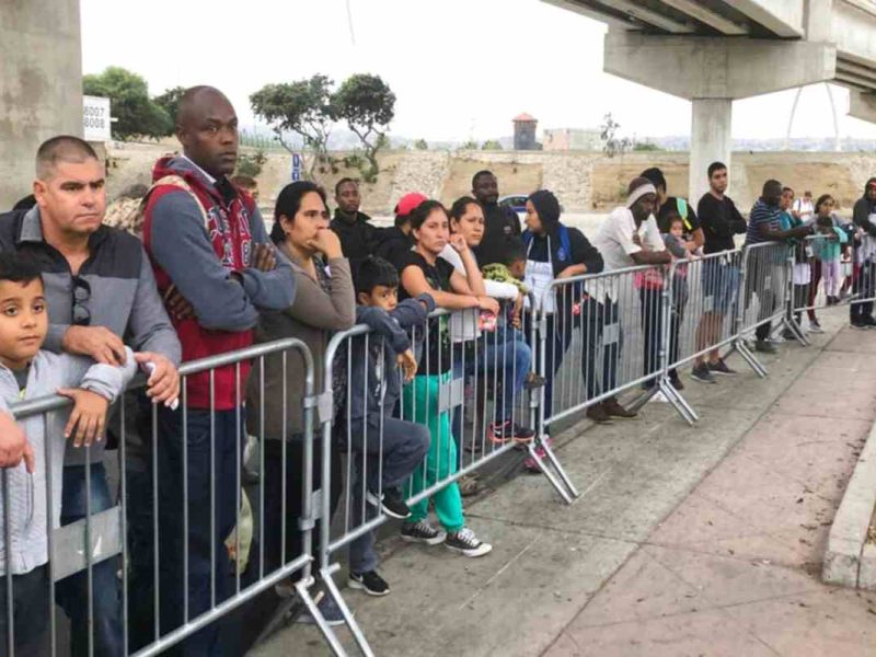 Solicitantes de asilo en Tijuana, México, escuchan si sus nombres son llamados en un cruce fronterizo en Estados Unidos tras el fin del programa Quédate en México.