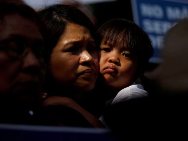 Un niño abraza a una mujer mientras la gente sostiene carteles para protestar contra la orden ejecutiva del presidente Donald Trump para detener y separar a las familias de los menores migrantes que cruzan la frontera.