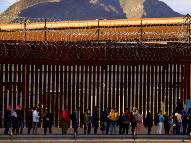 Migrantes hacen cola cerca de la valla fronteriza, después de cruzar el río Bravo, para solicitar asilo en Estados Unidos