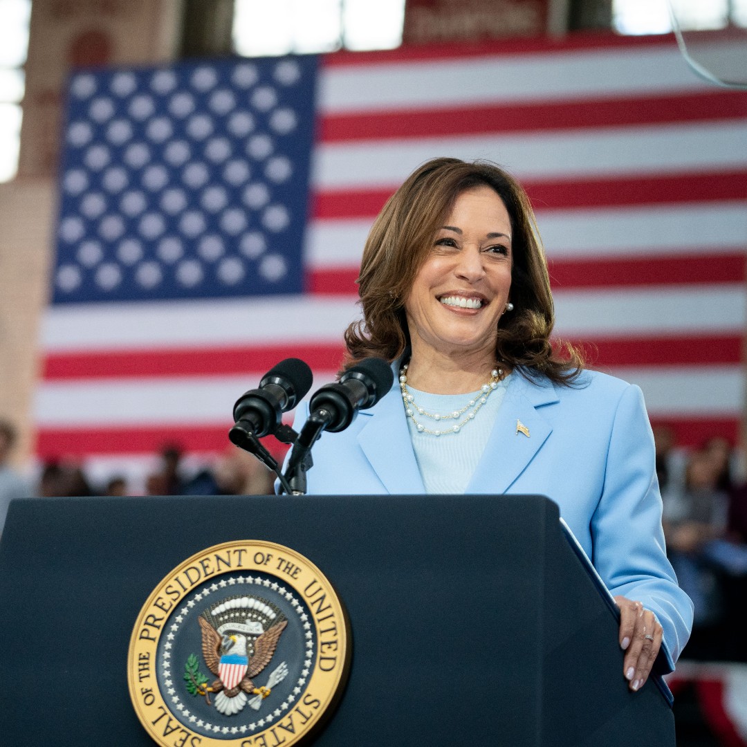 Vice President Kamala Harris standing behind a podium smiling. Behind her is the American flag.