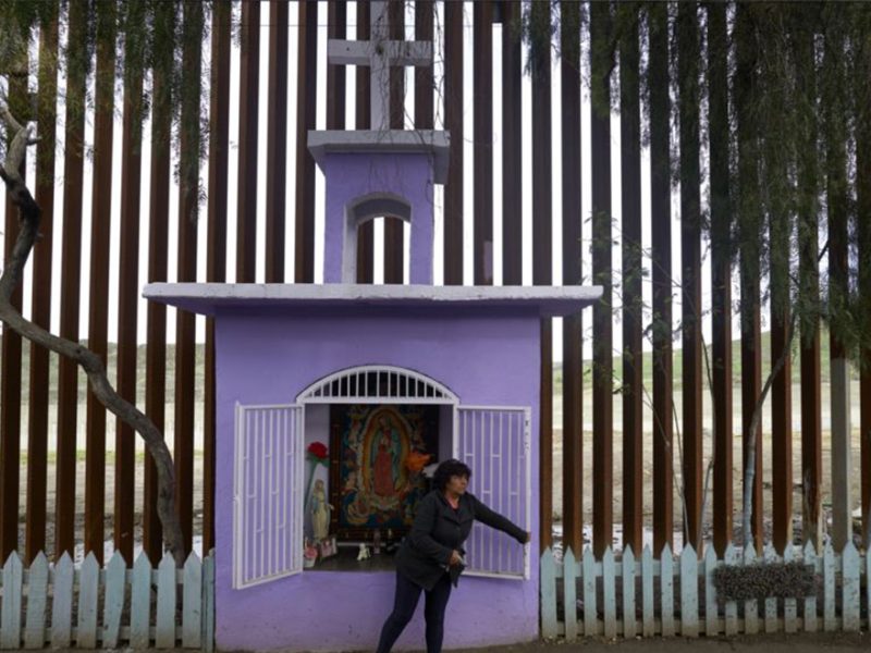 En esta foto de enero 16 de 2019, Esther Arias abre una ventana en una capilla construida por su padre José Arias delante de una renovada sección de una valla fronteriza de acero en Tijuana, México.