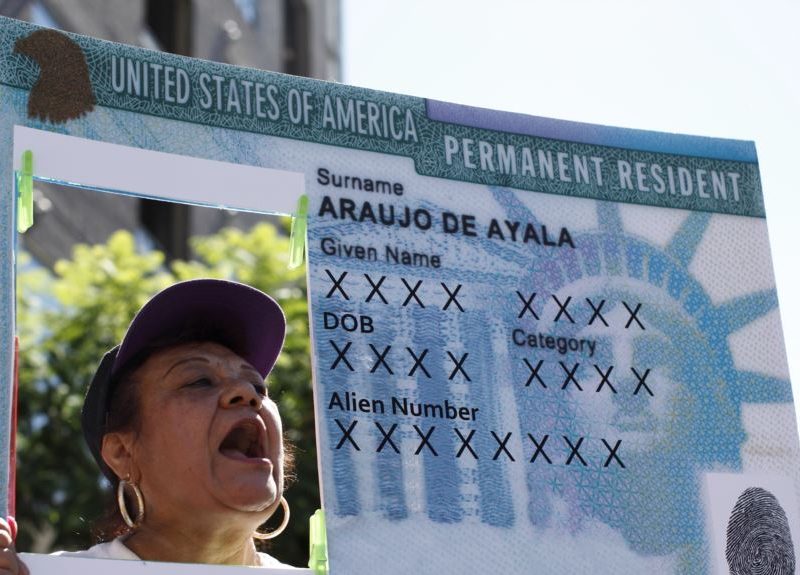 Imagen de archivo de una mujer levantando un cartel con una réplica de tarjeta de residencia.